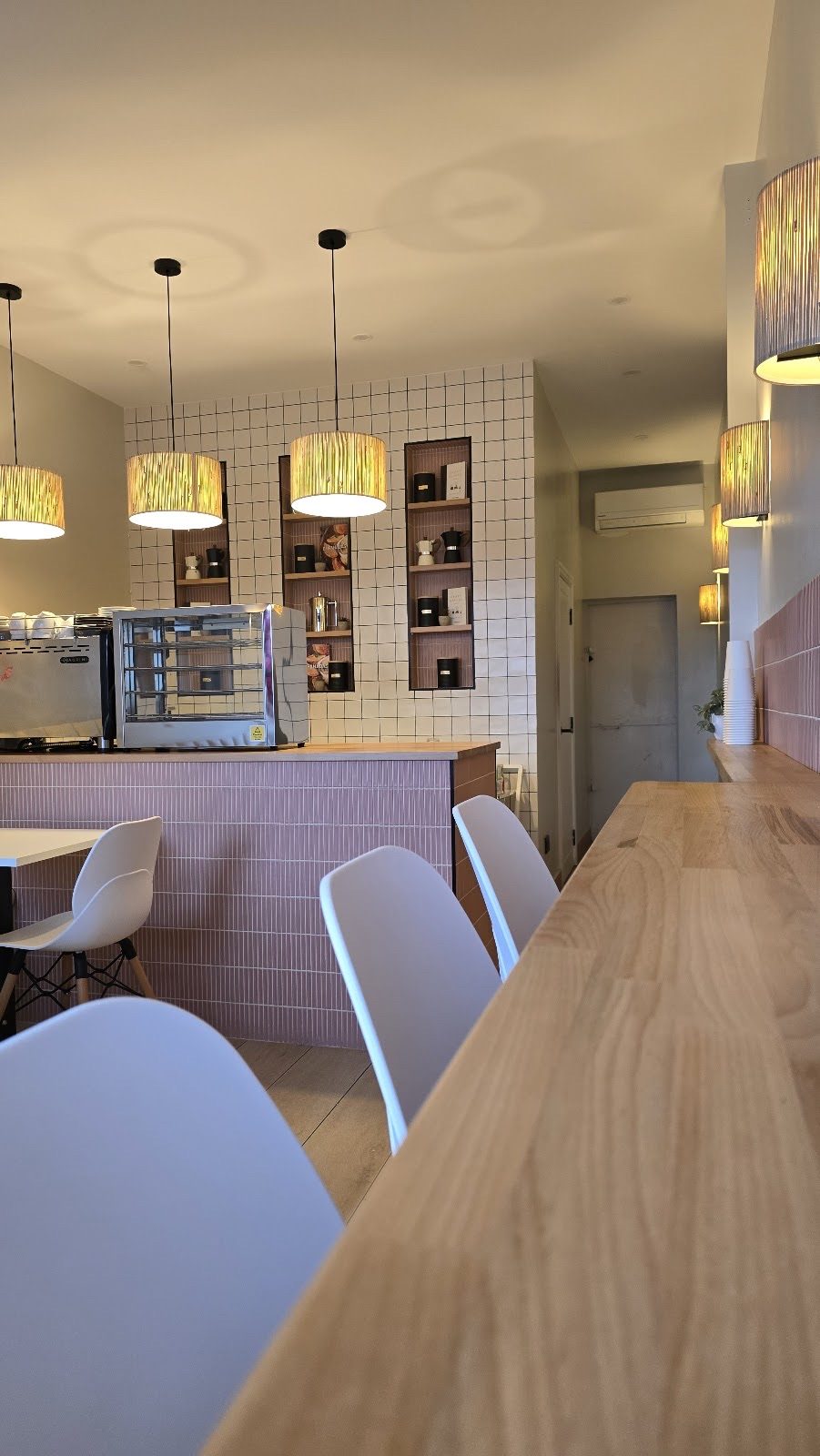 Looking towards the pastry counter and pink wall, wooden bench and white chairs in the foreground